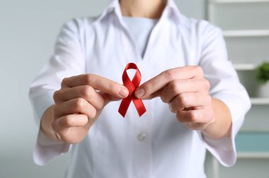 Doktor kırmızı farkındalık kurdelesini içeride tutuyor, yakın plan. Dünya AIDS Hastalıkları Günü