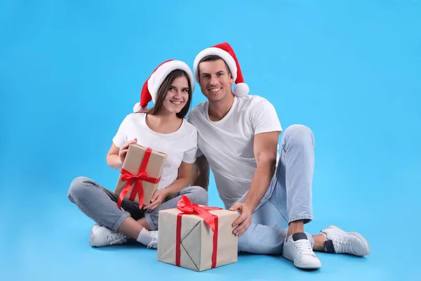 美しいです幸せなカップルでサンタ帽子に座ってクリスマスギフト上のライトブルーの背景 — ストック写真