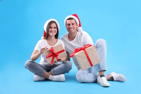 戴着圣诞礼帽 头戴浅蓝色背景圣诞礼物的年轻漂亮的夫妻 — 图库照片