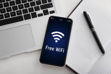 Akıllı telefon masadaki Wi-Fi 'ye bağlı. Laptop ve not defteri masada, düz yerde.