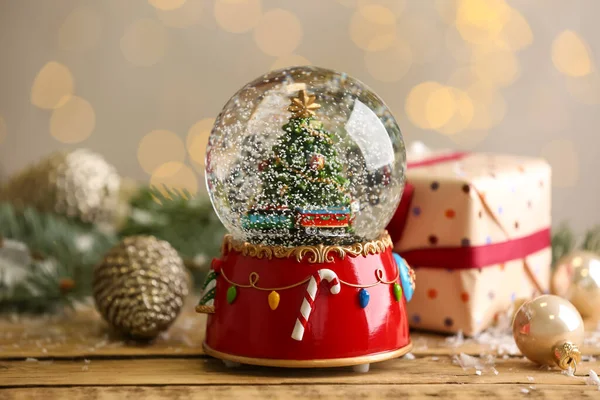 Beautiful snow globe with Christmas tree on wooden table against blurred festive lights