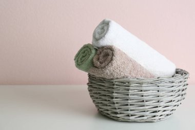 Pembe duvarın yanındaki gri masanın üzerinde temiz yumuşak havlular olan hasır sepet. Metin için boşluk