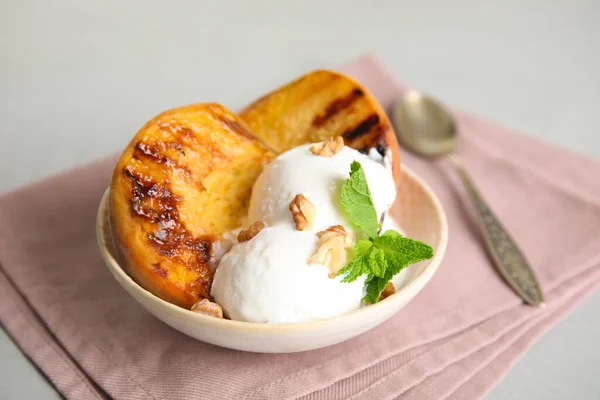 Delicious grilled peach with ice cream and walnuts on grey table