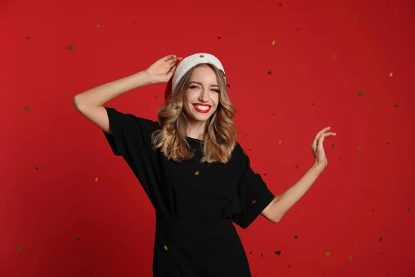 Szczęśliwa Młoda Kobieta Kapeluszu Mikołaja Konfetti Czerwonym Tle Święta Bożego — Zdjęcie stockowe