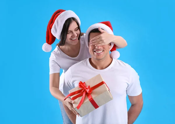 Woman presenting Christmas gift to boyfriend on light blue background