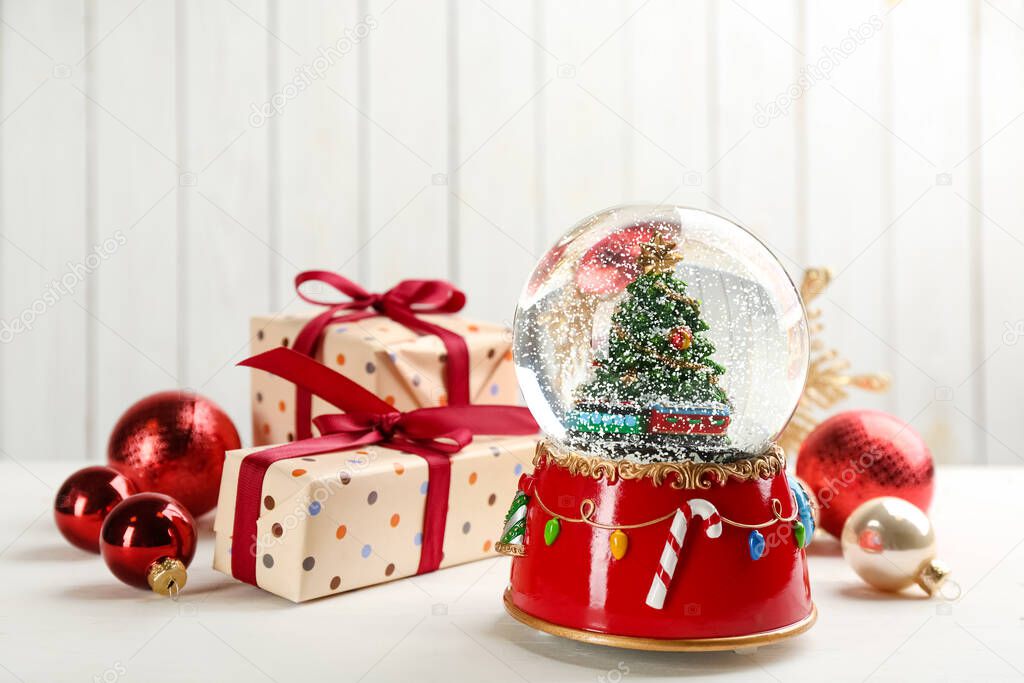 Beautiful snow globe, gift boxes and Christmas balls on white wooden table
