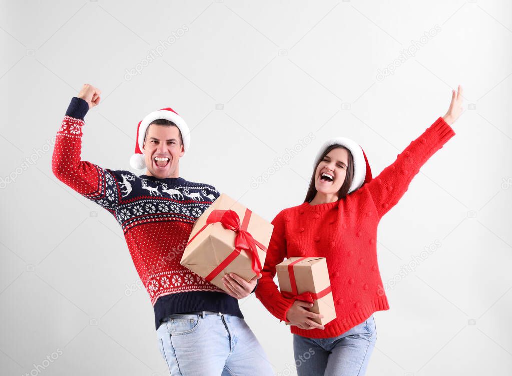 Beautiful happy couple in Santa hats with Christmas gifts having fun on light background