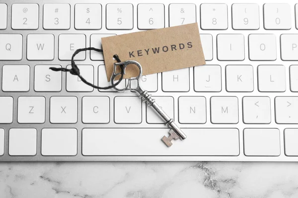 Keyboard, vintage key and tag with word KEYWORDS on white marble table, top view