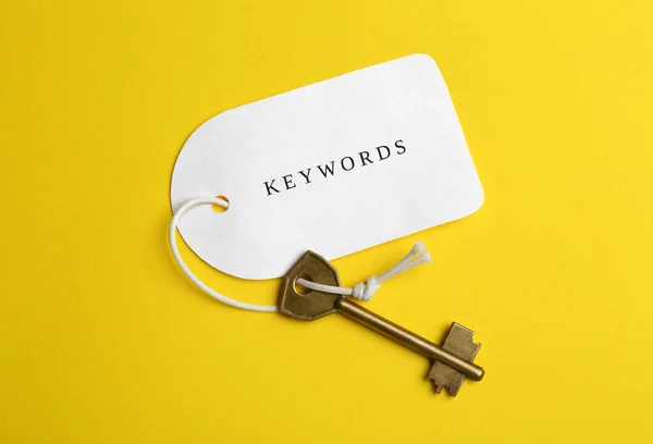 Metal key and tag wIth word KEYWORDS on yellow background, top view
