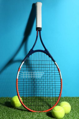 Tenis raketi ve toplar yeşil çimlerin üzerinde açık mavi arka plana karşı. Spor malzemeleri.