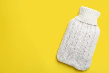 Sarı arka planda örülmüş sıcak su şişesi, üst manzara. Metin için boşluk