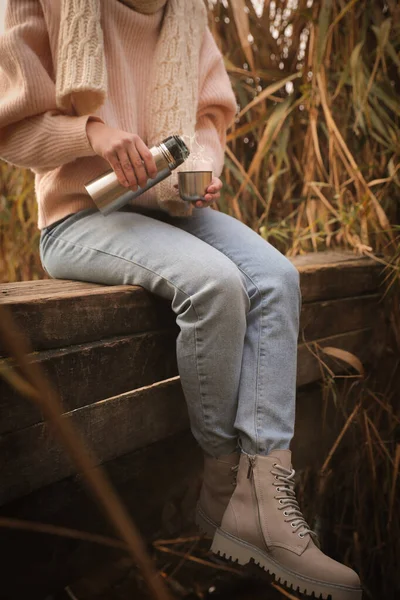 葦の間に木製の桟橋に座って魔法瓶を持つ女性 クローズアップ — ストック写真