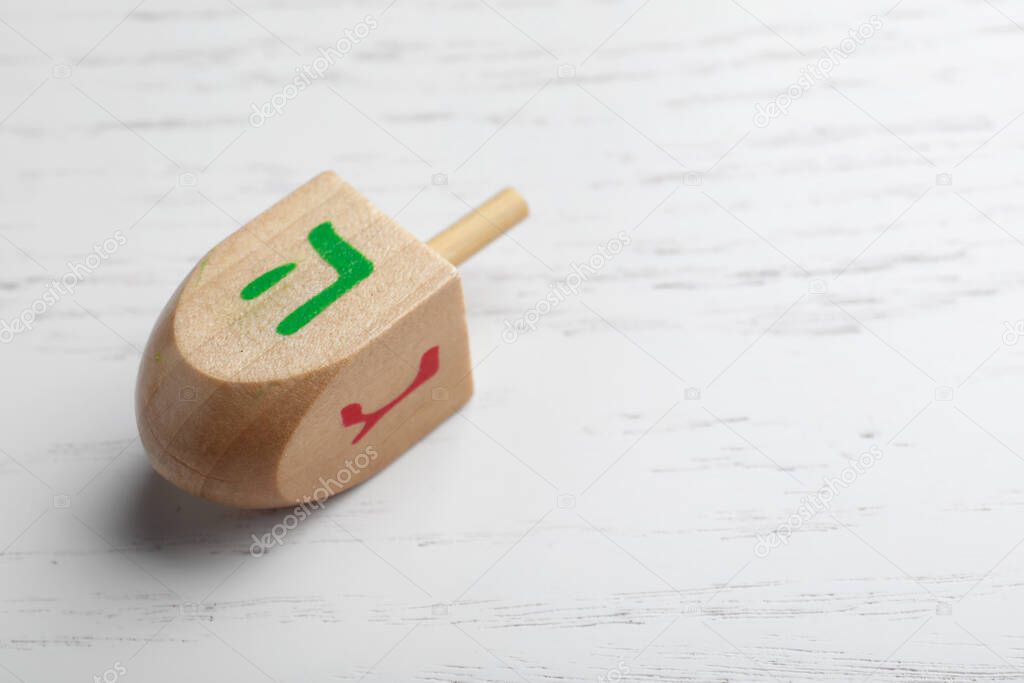Hanukkah traditional dreidel on white wooden background, closeup. Space for text