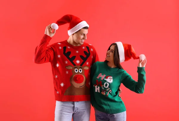 Hermosa Pareja Feliz Sombreros Santa Suéteres Navidad Sobre Fondo Rojo —  Fotos de Stock
