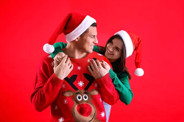 Hermosa Pareja Feliz Sombreros Santa Suéteres Navidad Sobre Fondo Rojo —  Fotos de Stock