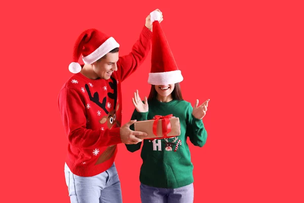 Mann Überreicht Seiner Freundin Weihnachtsgeschenk Auf Rotem Hintergrund — Stockfoto