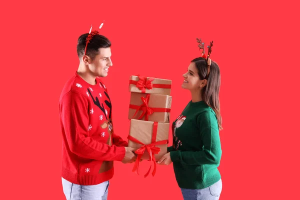 漂亮而快乐的一对 戴着圣诞头巾 穿着红色背景的毛衣 带着礼物 — 图库照片