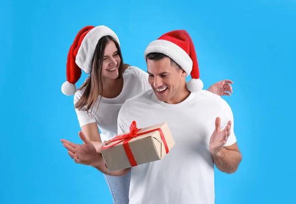 Woman presenting Christmas gift to boyfriend on light blue background