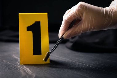 Siyah tahta masada, kanıt işaretinin yakınından kovan alan kadın, yakın plan. Suç mahalli