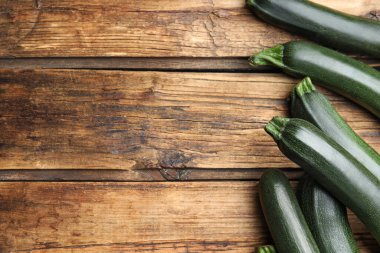 Ahşap masanın üzerinde yeşil olgun kabaklar, düz uzanmış. Metin için boşluk