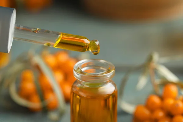 Natural sea buckthorn oil dripping from pipette into bottle on blurred background, closeup