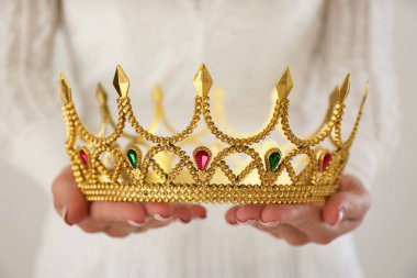 Elinde parlak arka planda mücevherleri olan güzel bir taç tutan kadın, yakın plan. Fantezi ortaçağ dönemi