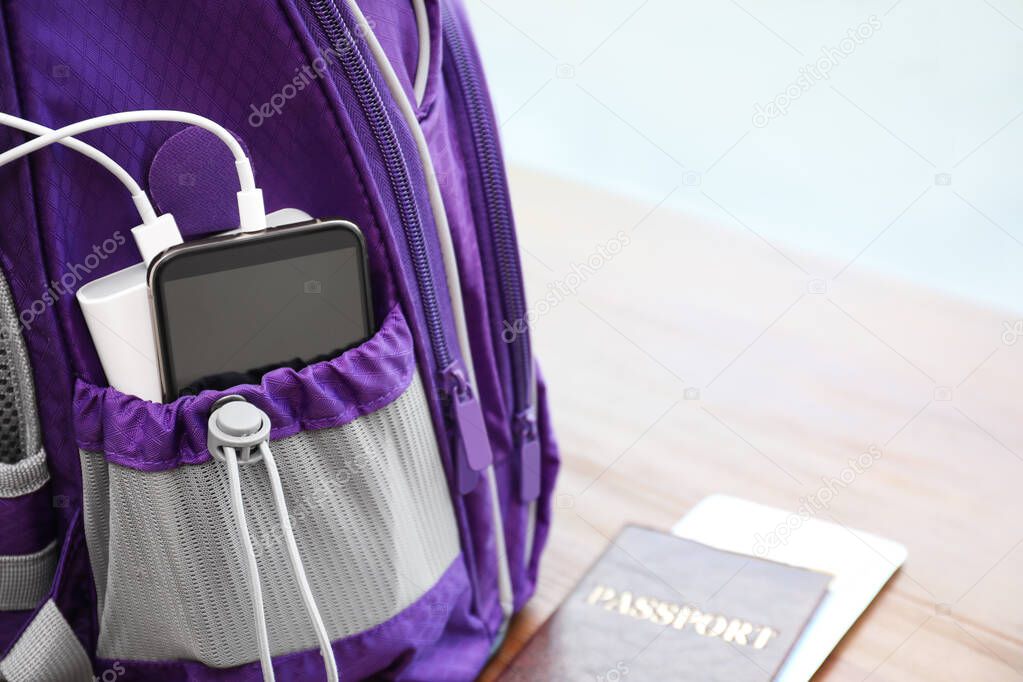 Charging mobile phone with power bank in purple backpack and passport on table, closeup. Space for text