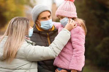 Sonbahar günü dışarıda maskeli bir aile. Koronavirüs karantinası sırasında koruyucu tedbirler