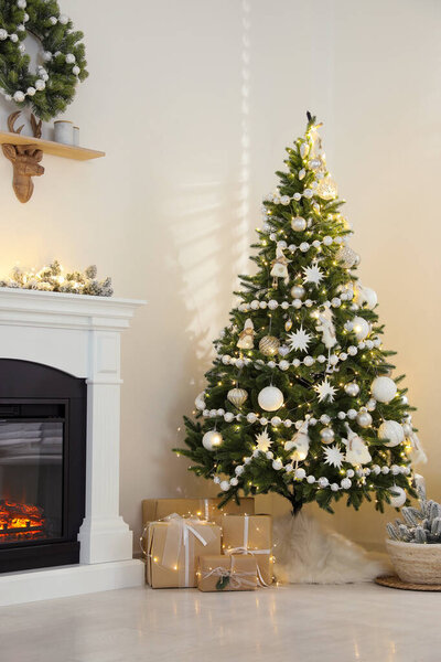 Decorated Christmas tree with faux fur skirt and gift boxes near fireplace indoors