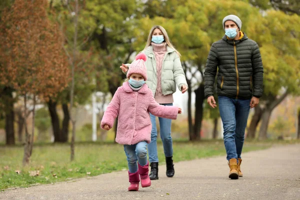 Family in medical masks walking outdoors on autumn day. Protective measures during coronavirus quarantine