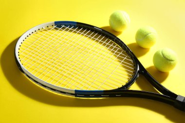 Tenis raketi ve toplar sarı arka planda. Spor malzemeleri.