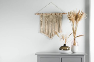 Reed 'in çiçekleri gri dolapta cam vazolarda, dekoratif elementlerle birlikte beyaz duvarın yanında. Metin için boşluk