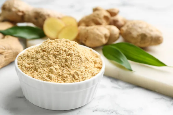 Dry ginger powder and fresh root on white marble table. Space for text