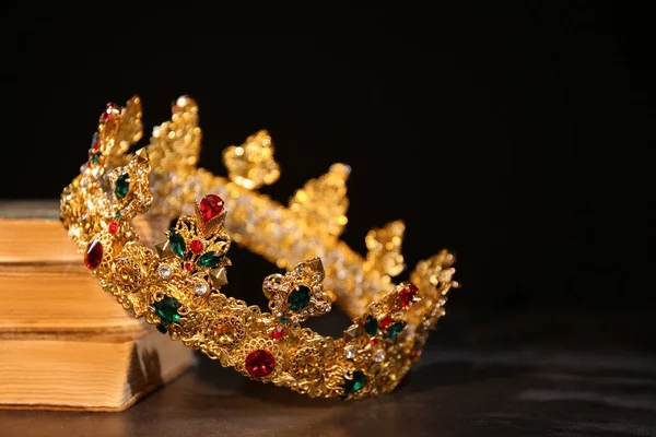 Beautiful golden crown and old books on black table. Fantasy item