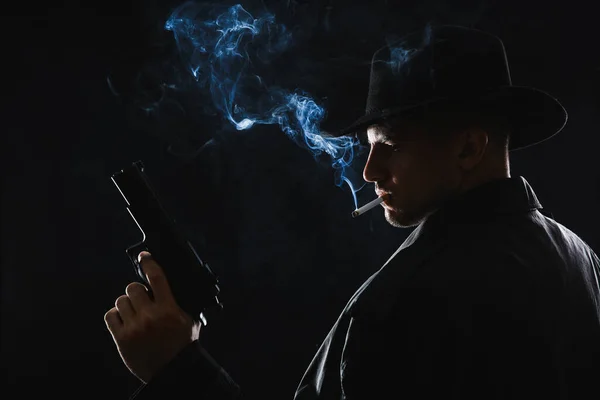Old fashioned detective with gun smoking cigarette on dark background