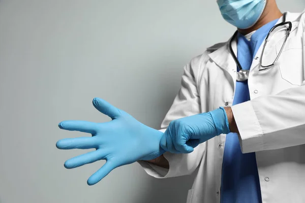 Dokter Beschermende Masker Zetten Medische Handschoenen Tegen Lichtgrijze Achtergrond Close — Stockfoto