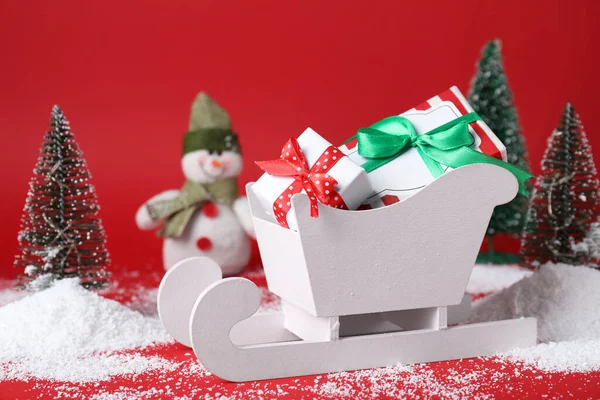 Schlitten Mit Geschenkschachteln Und Weihnachtsdekoration Auf Rotem Hintergrund — Stockfoto