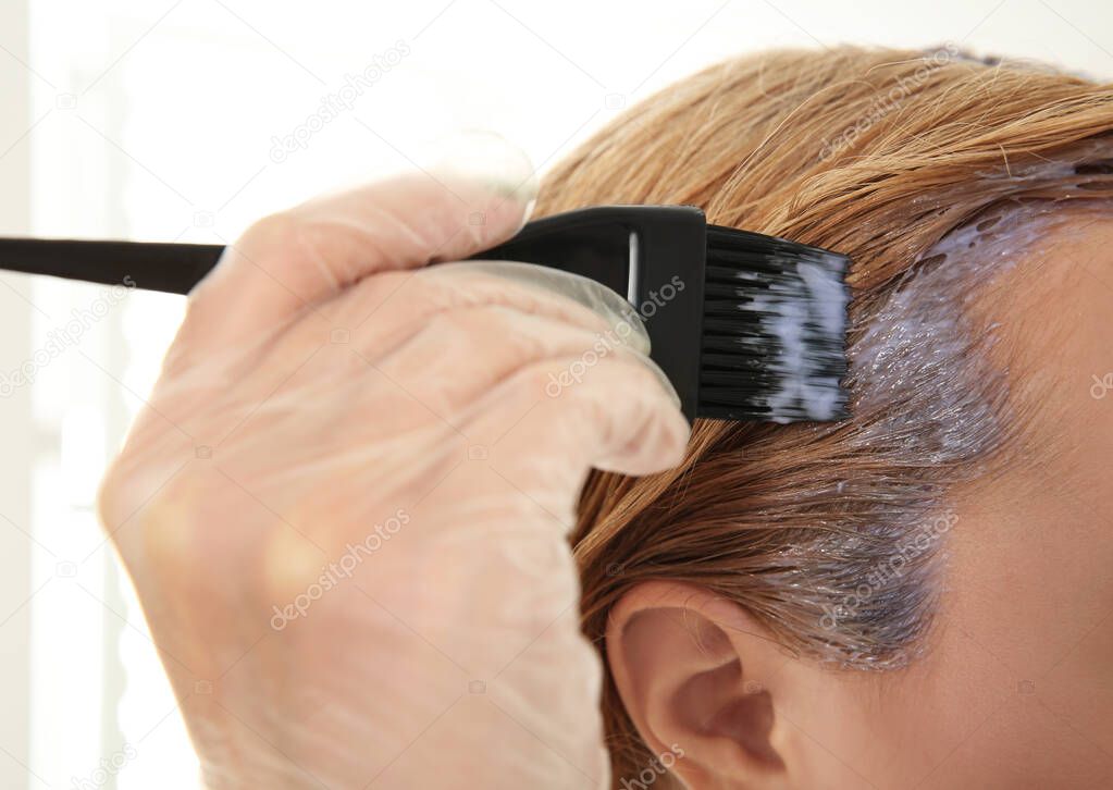 Young woman applying dye on hairs indoors, closeup