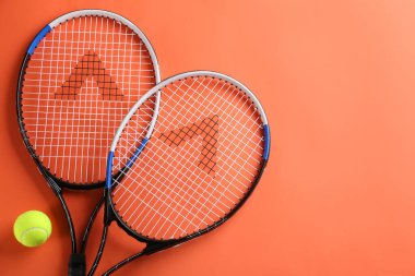 Tenis raketleri ve top turuncu arka planda, düz yerde. Metin için boşluk