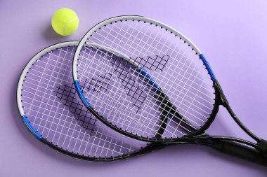 Tenis raketleri ve top menekşe arka planda, düz yerde. Spor malzemeleri.