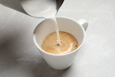 Gri masadaki kahve fincanına süt dökülüyor, yakın plan.