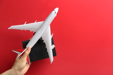 Kırmızı arka planda oyuncak uçak ve pasaport taşıyan kadın, yakın plan. Metin için boşluk