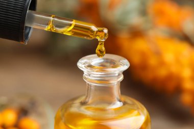 Natural sea buckthorn oil dripping from pipette into bottle on blurred background, closeup clipart