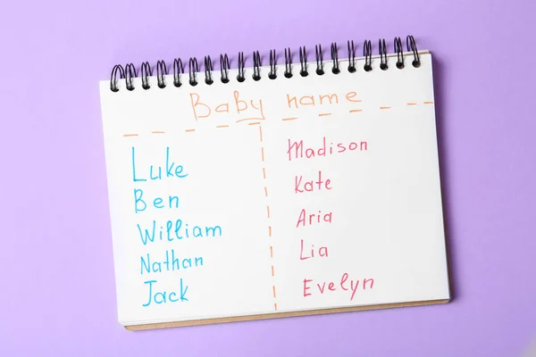 Notebook with lists of baby names on purple background, top view