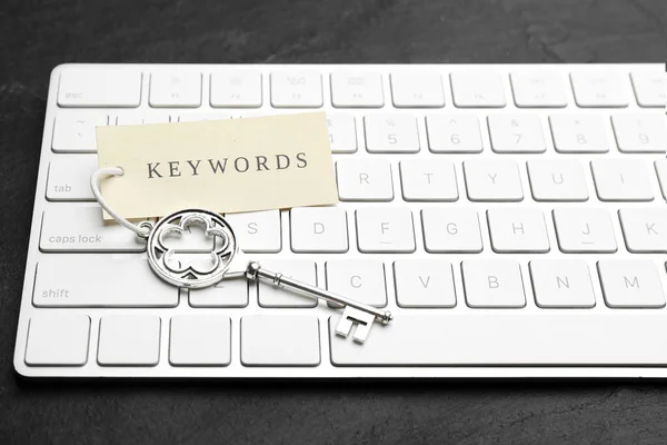 Keyboard, vintage key and tag with word KEYWORDS on black table, closeup