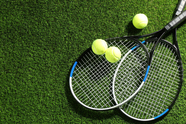 Tennis rackets and balls on green grass, flat lay. Space for text