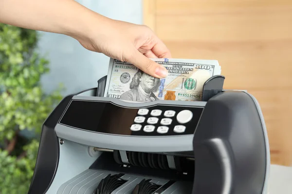 Woman putting money into counting machine indoors, closeup