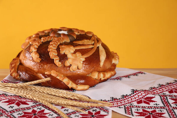 Rushnyk with korovai, wheat spikes on yellow background. Ukrainian bread and salt welcoming tradition
