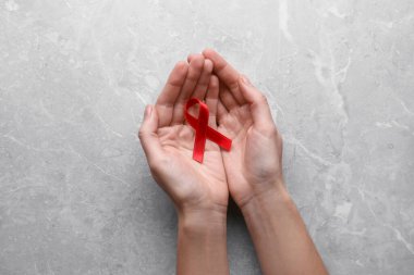 Açık gri mermer masada kırmızı farkındalık kurdelesi tutan kadın. Dünya AIDS Hastalıkları Günü