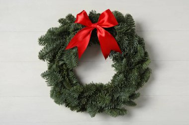 Noel çelengi, köknar ağacı dallarından yapılmıştır. Beyaz ahşap arka planda kırmızı kurdele vardır.